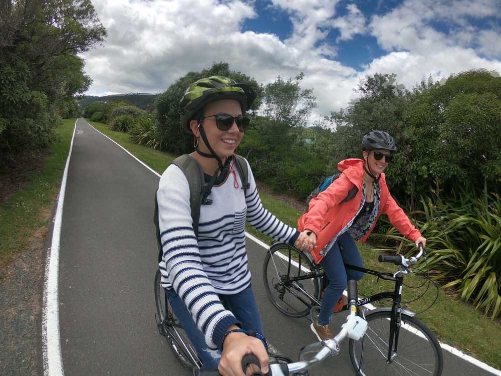 Viajar a Nueva Zelanda dos chicas cogidas de la mano y montadas en una bicicleta